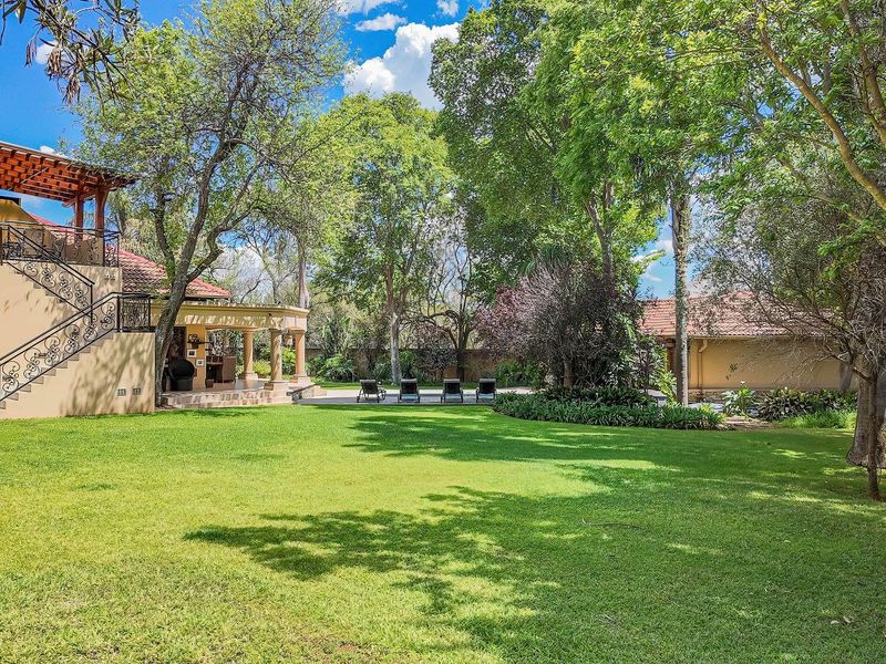 Spacious rear garden featuring a well-maintained lawn, mature trees, and a covered patio area with an external staircase leading to an upper balcony.