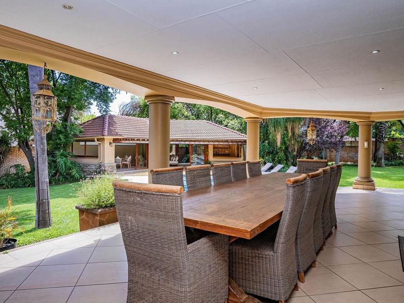 Spacious covered patio featuring tiled flooring and structural columns, overlooking a well-maintained garden and secondary outdoor structure.