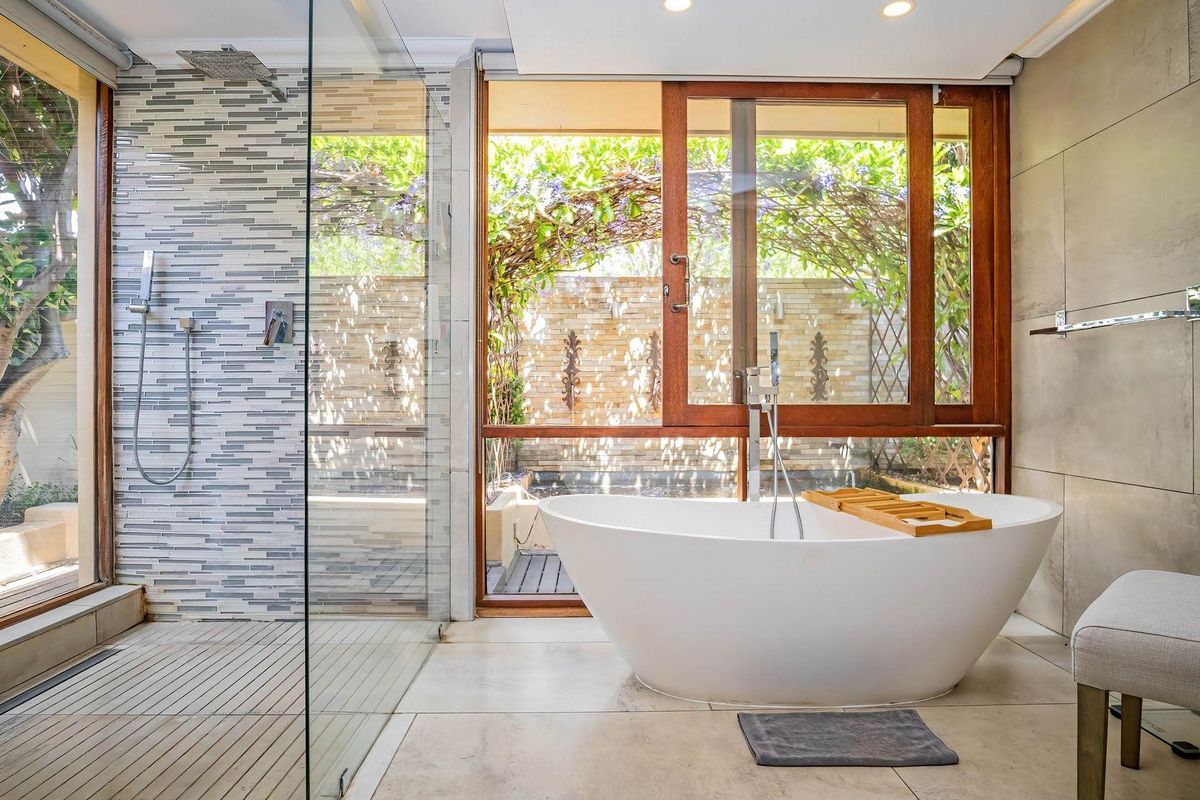 Modern bathroom featuring a freestanding bathtub, spacious walk-in shower with mosaic tiling, and large timber-framed windows overlooking a private garden area.