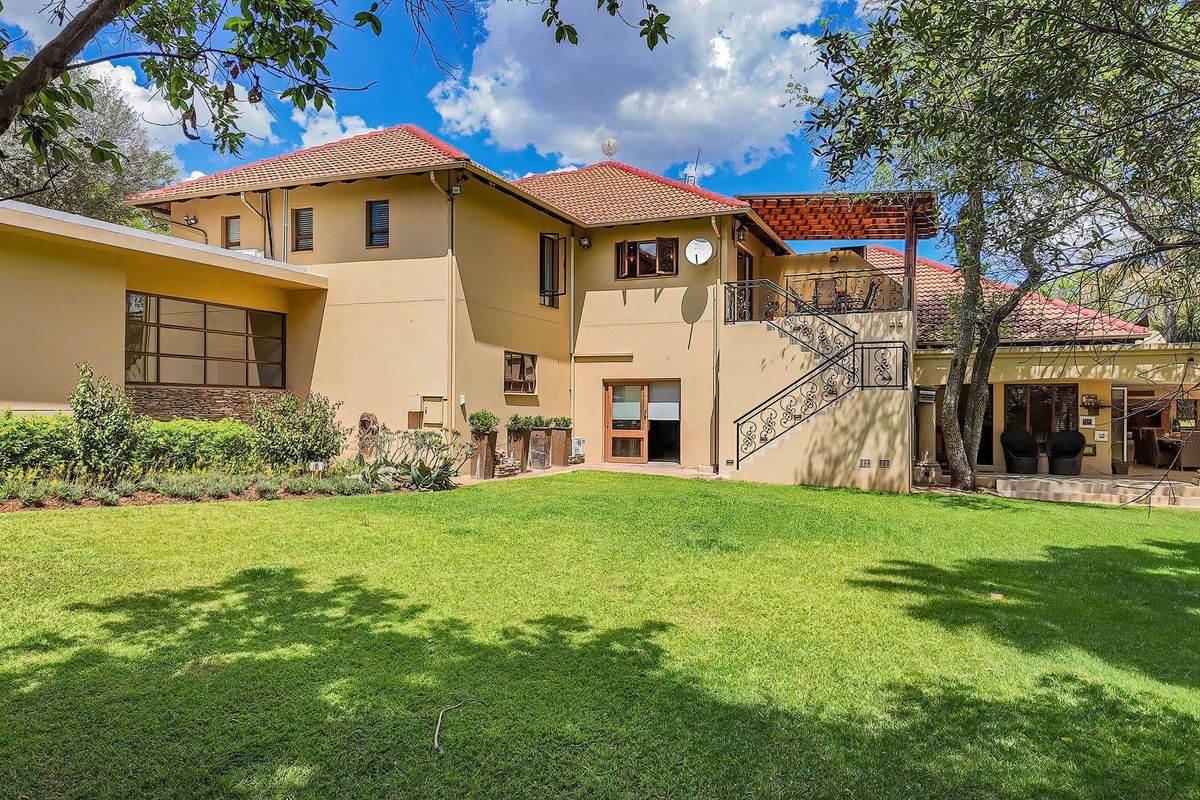 Rear view of a spacious farm-style residence featuring a well-maintained lawn, stone patio, wooden pergola, and an elegant wrought iron staircase.