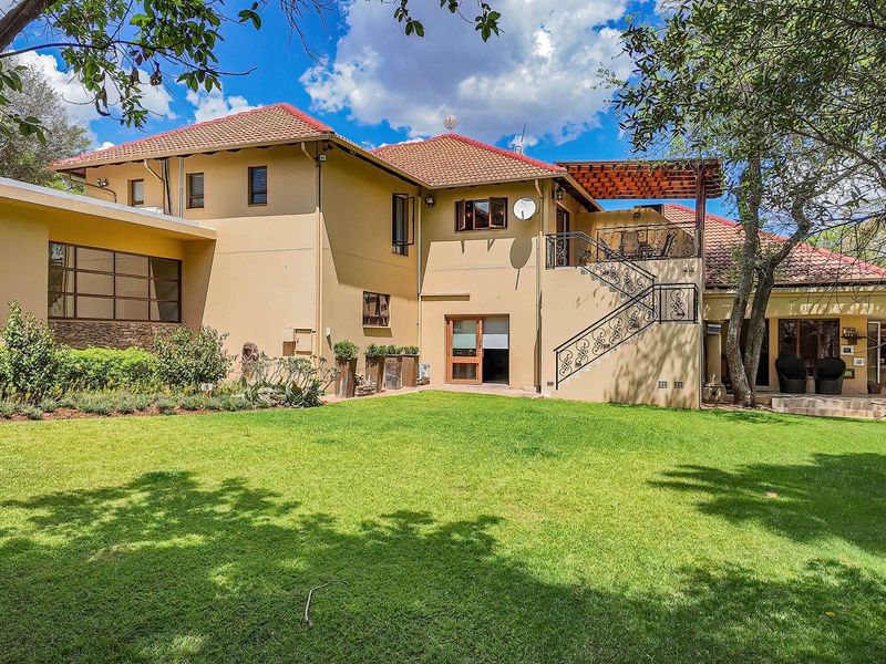 Rear view of a spacious farm-style residence featuring a well-maintained lawn, stone patio, wooden pergola, and an elegant wrought iron staircase.