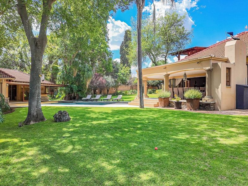 Spacious rear garden featuring a well-maintained lawn, a swimming pool, and a large covered patio area with stone-clad columns.