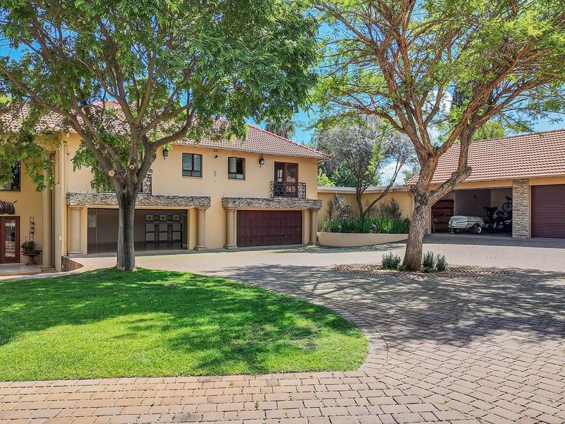 Spacious front exterior of a farm property featuring a large paved driveway, mature trees, landscaped garden, and multiple garage bays with stone-clad accents.