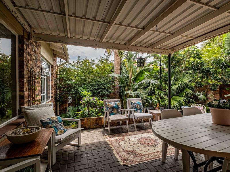 A covered outdoor patio featuring brick paving, a corrugated metal roof, and a lush garden outlook, providing a comfortable space for outdoor relaxation.