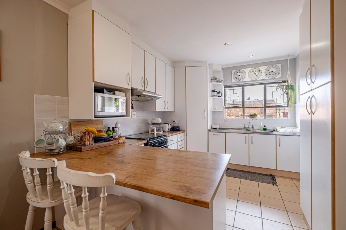 A functional kitchen featuring white cabinetry, a wooden breakfast bar, tiled flooring, and a stainless steel sink with a tiled backsplash.