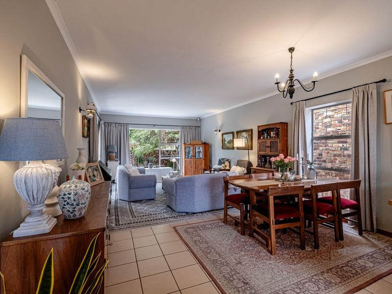 Spacious open-plan living and dining area featuring tiled floors, elegant chandelier lighting, and a large sliding door leading to the garden.