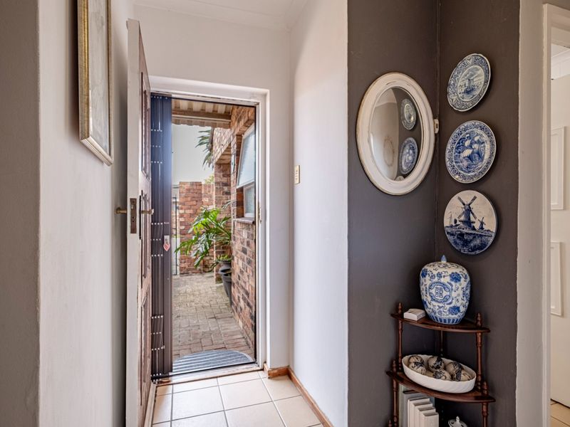 A welcoming entrance hall featuring tiled flooring and a timber front door with an integrated security gate, leading to an outdoor paved area.