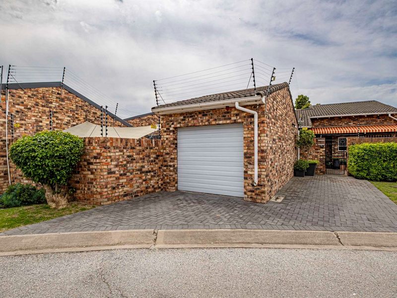 Front view of a face brick property featuring a single garage, paved driveway, and secure electric fencing.