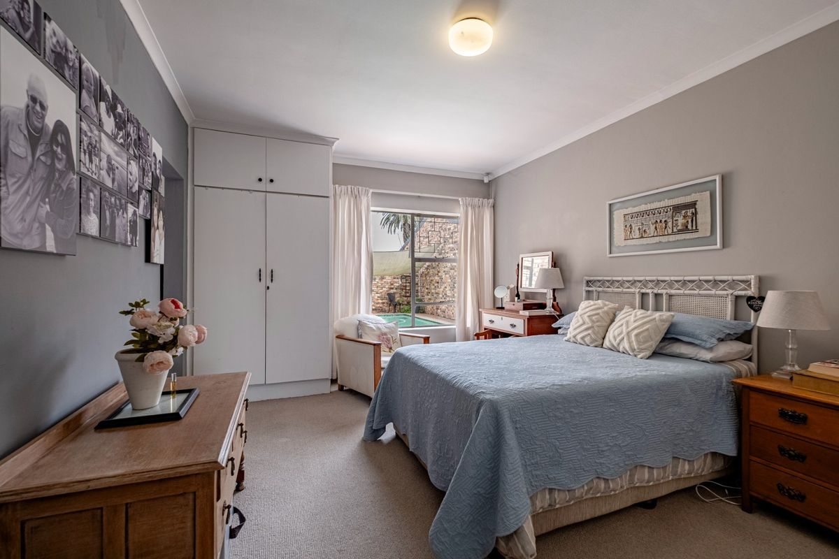 A well-lit bedroom featuring built-in wardrobes, carpeted flooring, and a window view overlooking the pool area.