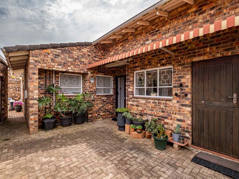 A charming rear courtyard featuring classic face brick walls, a paved patio area, and a traditional timber stable door with a striped retractable awning.