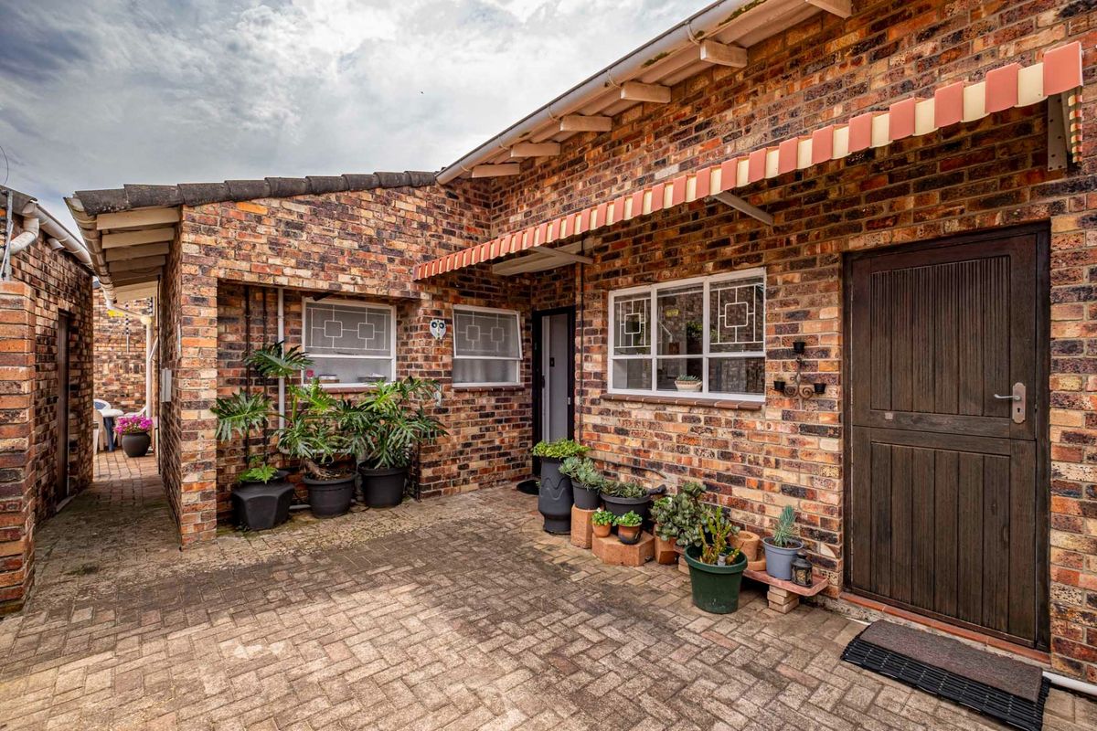 A charming rear courtyard featuring classic face brick walls, a paved patio area, and a traditional timber stable door with a striped retractable awning.