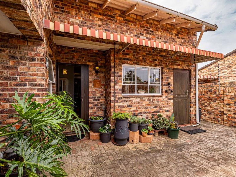A charming covered patio area featuring classic face brick walls, paved flooring, and a retractable awning, providing a cozy outdoor space.