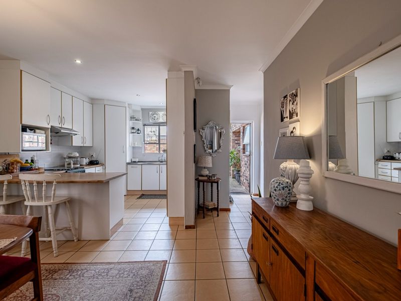Open plan kitchen and dining area featuring tiled flooring, white cabinetry, and a breakfast counter, leading to a rear exterior entrance.