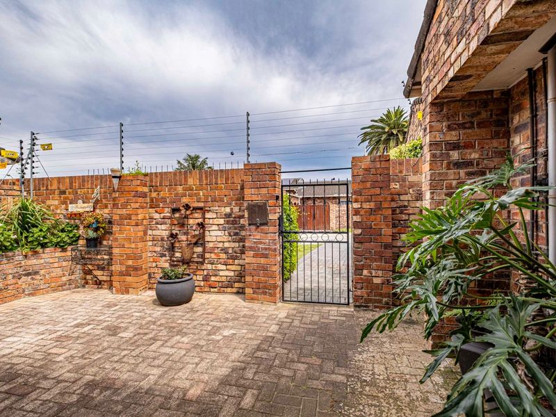 Front entrance area featuring a secure brick boundary wall with electric fencing and a paved driveway leading to a metal pedestrian gate.