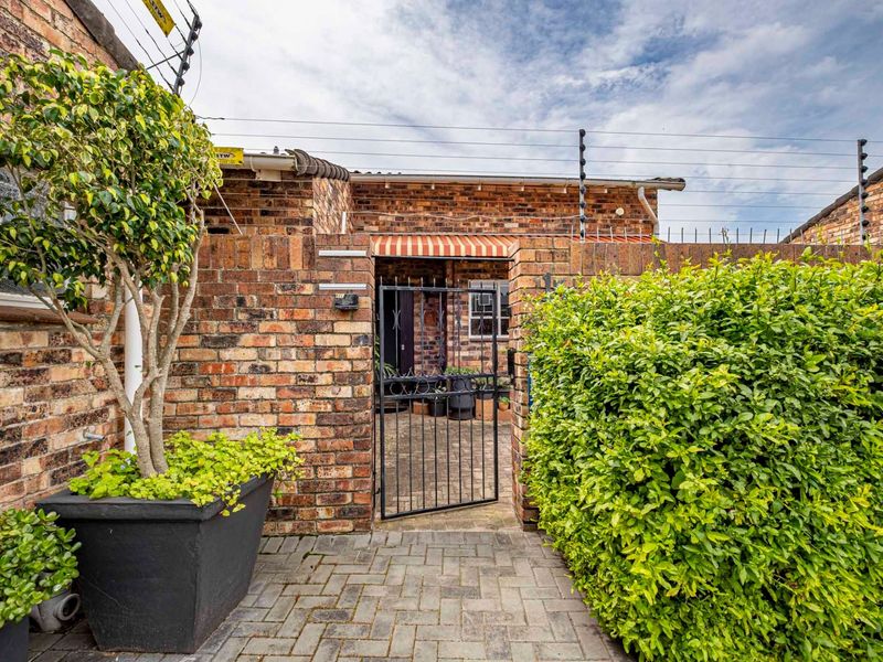 A secure front entrance featuring a face brick facade, paved walkway, and metal security gate with electric fencing.