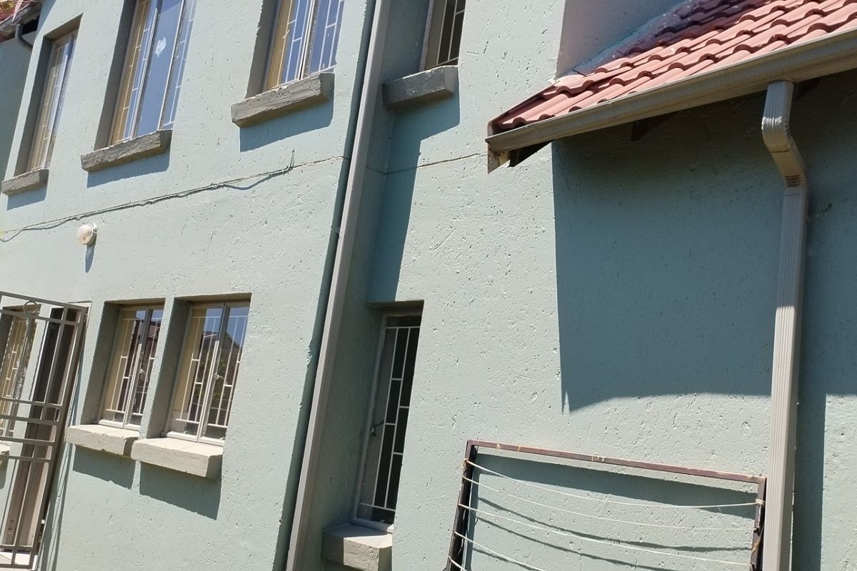 Rear exterior view of a townhouse featuring plastered walls, terracotta roof tiles, and security fixtures on windows and doors.