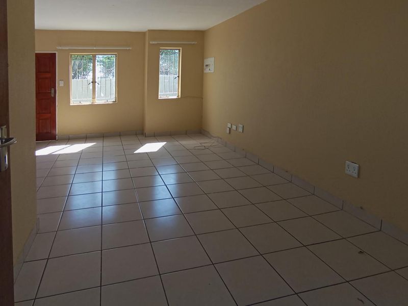 A spacious, empty living area featuring neutral tiled flooring, large windows with security bars, and a solid timber entrance door.