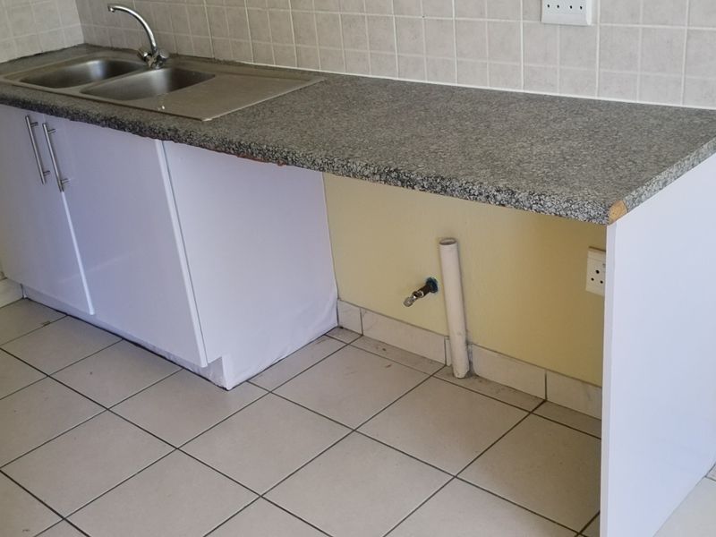 A basic kitchen area featuring a stainless steel sink, laminate countertop, and tiled backsplash, currently empty and requiring minor repairs to finishes.