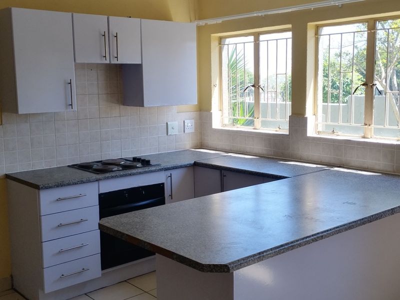 A functional kitchen featuring white cabinetry, laminate countertops, a built-in oven and hob, and tiled backsplash with natural light from dual windows.
