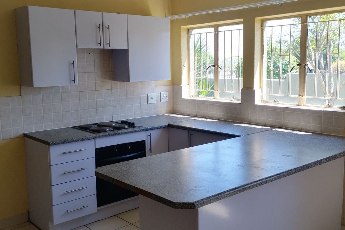 A functional kitchen featuring white cabinetry, laminate countertops, a built-in oven and hob, and tiled backsplash with natural light from dual windows.
