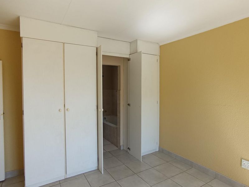 A bright, empty bedroom featuring tiled flooring and built-in cupboards, with an adjoining bathroom visible through the doorway.