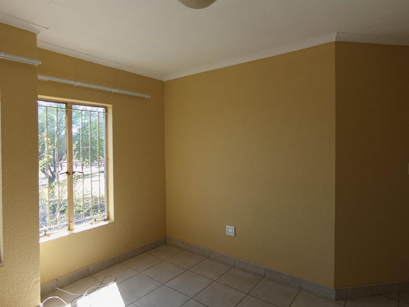 An empty bedroom featuring tiled flooring, coved ceilings, and windows fitted with security bars, offering a blank canvas for personalization.