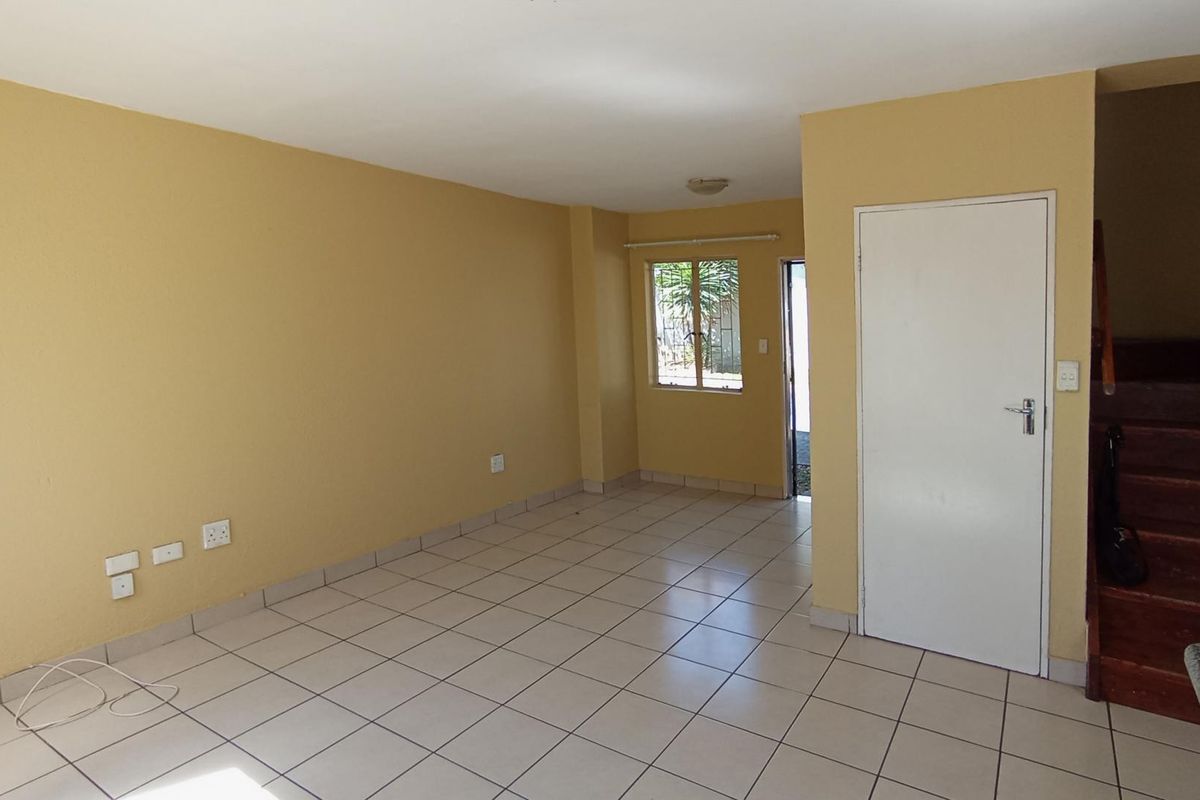 An empty, open-plan living area featuring tiled flooring, neutral wall paint, and a wooden staircase leading to the upper level.