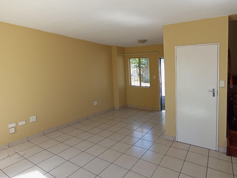 An empty, open-plan living area featuring tiled flooring, neutral wall paint, and a wooden staircase leading to the upper level.