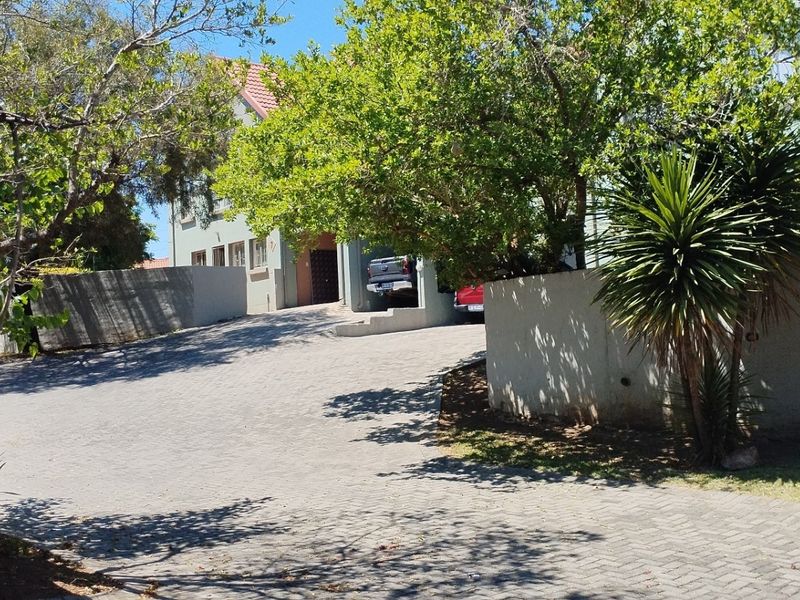 Front view of the townhouse property featuring a paved driveway, boundary wall, and covered parking area.