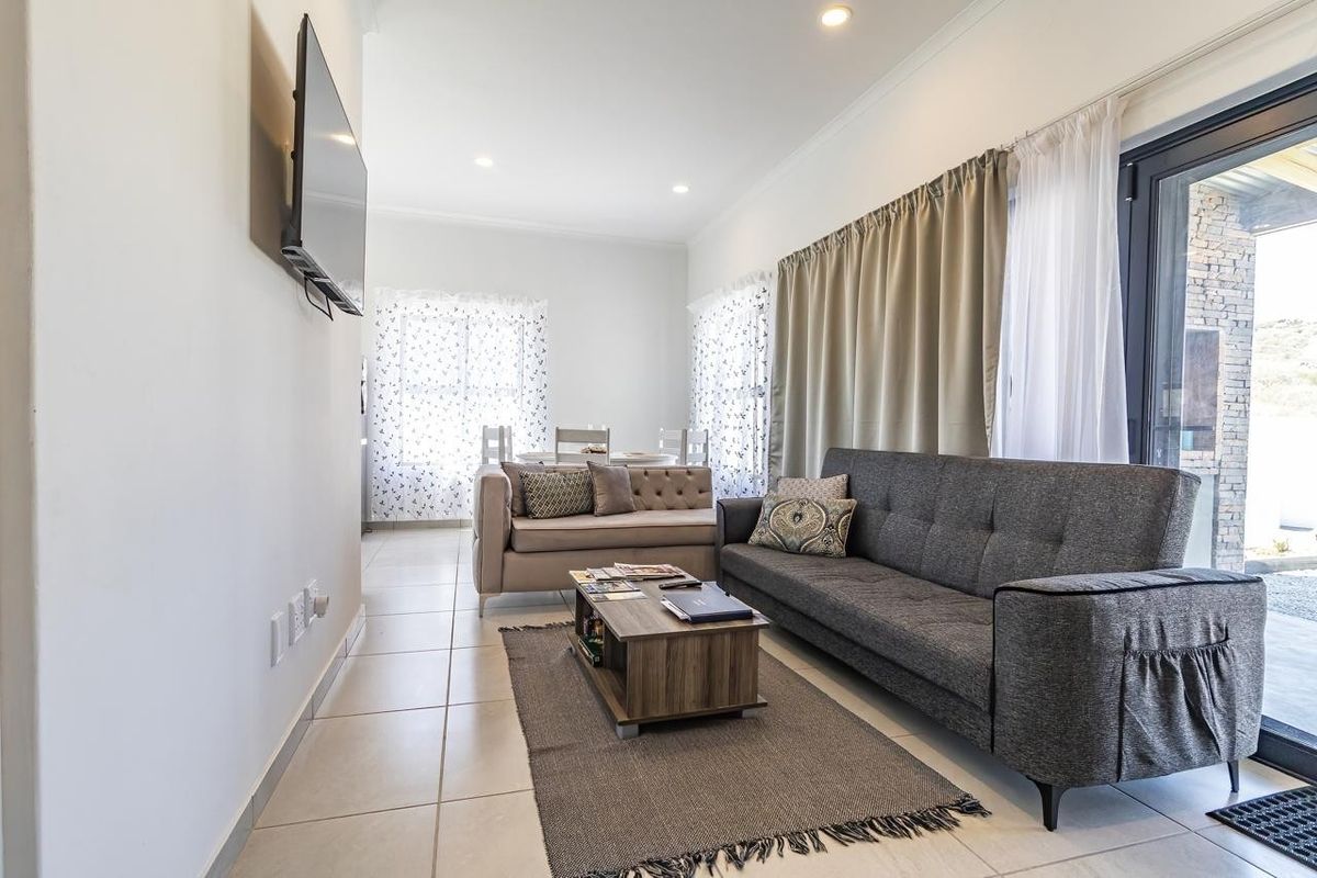 A bright and open living room featuring tiled flooring, recessed downlights, and a large sliding glass door providing access to the outdoor area.