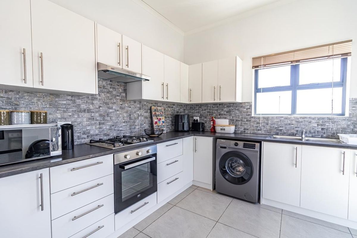 Modern kitchen featuring white cabinetry, dark countertops, a gas hob with extractor, built-in oven, and integrated laundry space with tiled flooring.