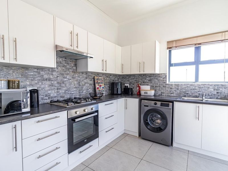 Modern kitchen featuring white cabinetry, dark countertops, a gas hob with extractor, built-in oven, and integrated laundry space with tiled flooring.