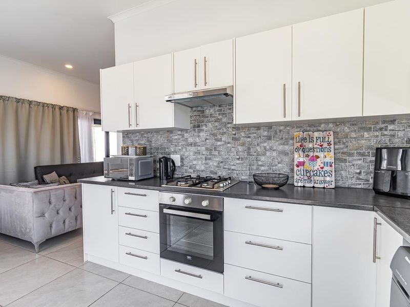 Modern open-plan kitchen featuring white cabinetry, stone-look tile backsplash, built-in oven, gas hob, and sleek laminate countertops, seamlessly flowing into the living area.