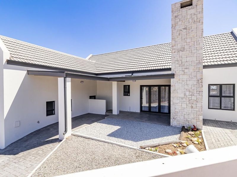 A modern rear exterior view featuring a stone-clad chimney, covered patio area, paved driveway, and well-maintained landscaping.