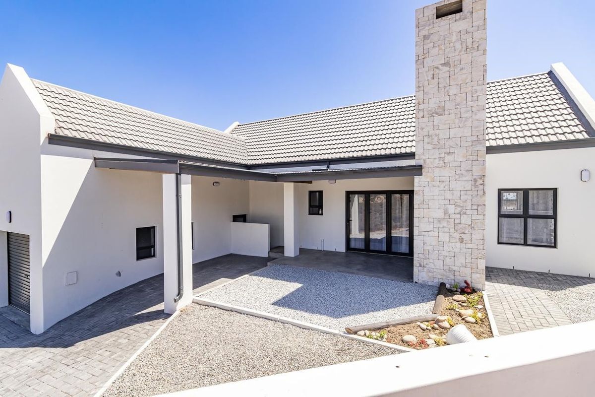 A modern rear exterior view featuring a stone-clad chimney, covered patio area, paved driveway, and well-maintained landscaping.