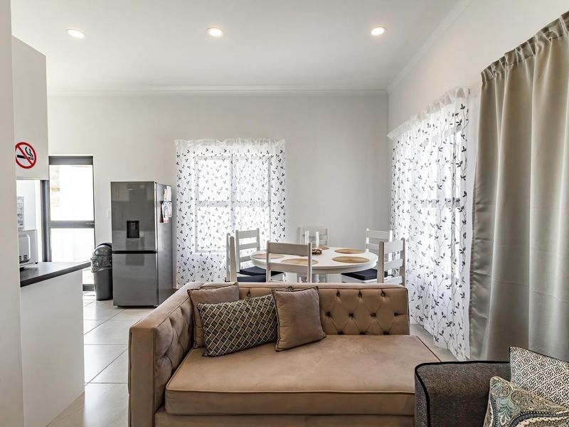 An open-plan living and dining area featuring neutral tiled flooring, recessed ceiling lighting, and large windows with natural light.