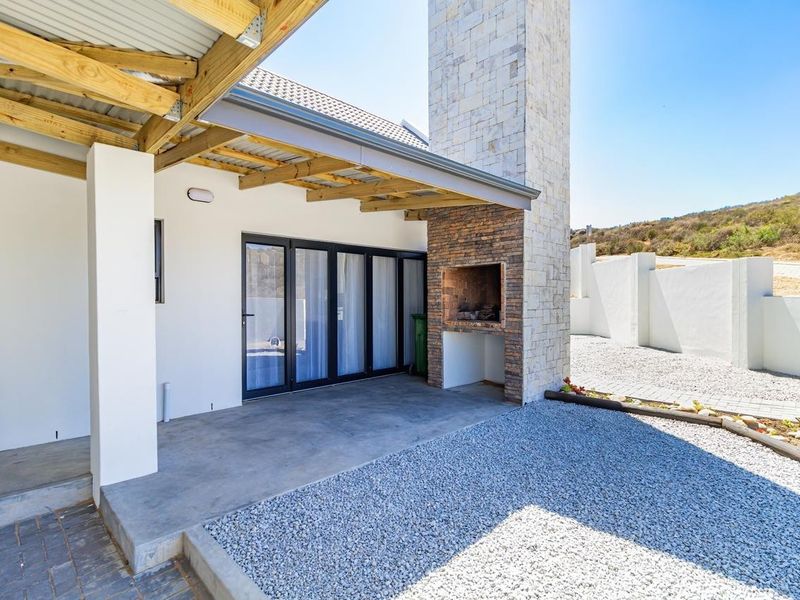 Covered patio area featuring a built-in braai with a stone-clad chimney, concrete flooring, and direct access to the interior via sliding glass doors.