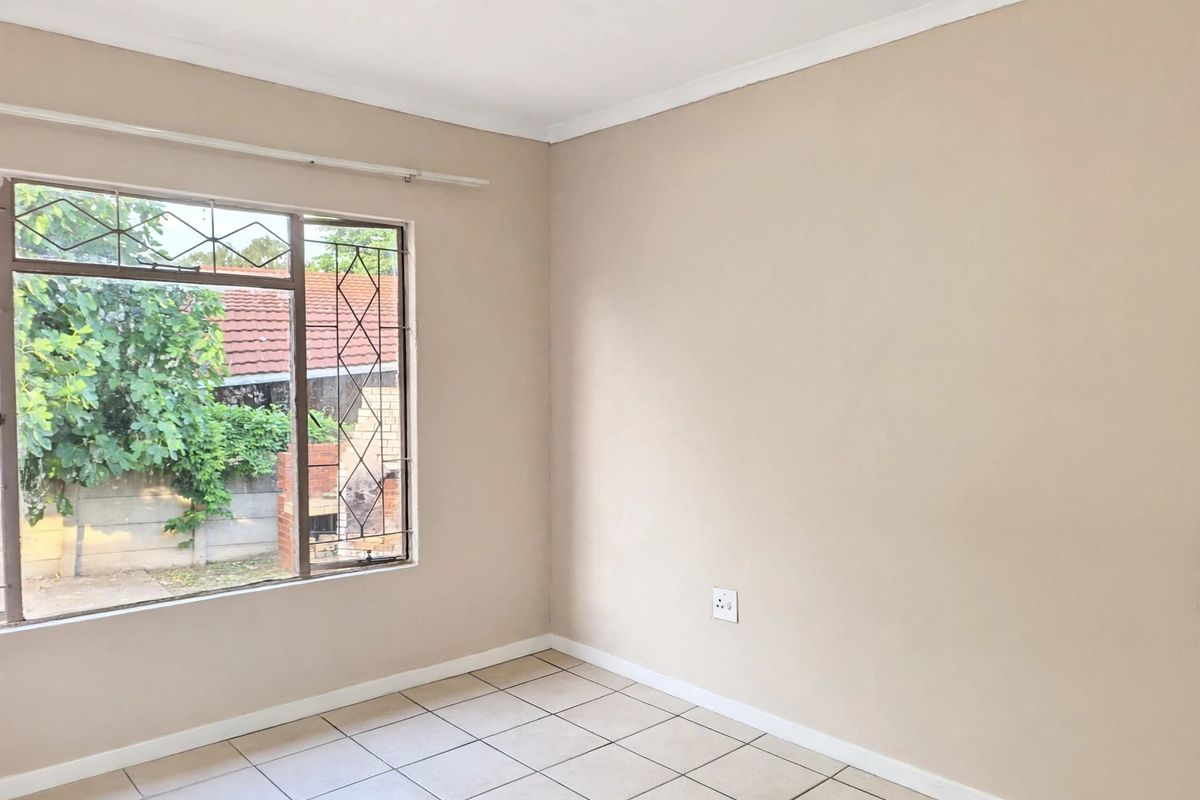 A clean, empty bedroom featuring neutral wall paint, tiled flooring, and a window fitted with security bars.