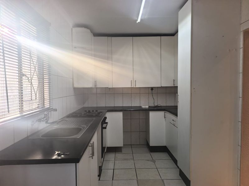 A functional kitchen featuring white cabinetry, dark countertops, built-in oven and hob, tiled splashbacks, and tiled flooring, offering a clean canvas for updates.