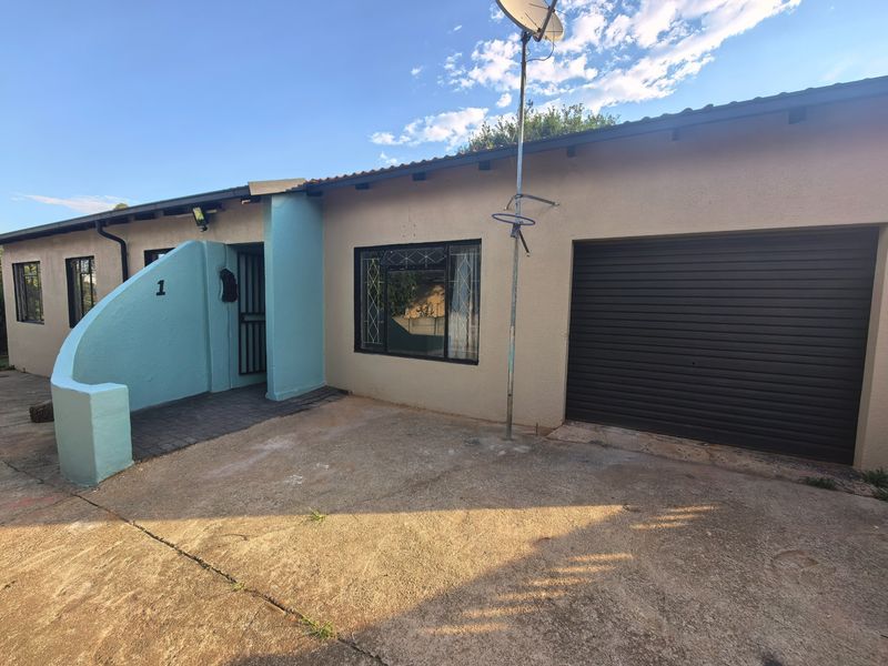 Front exterior view of the property featuring a single garage, concrete driveway, and a covered entrance area with security gate.