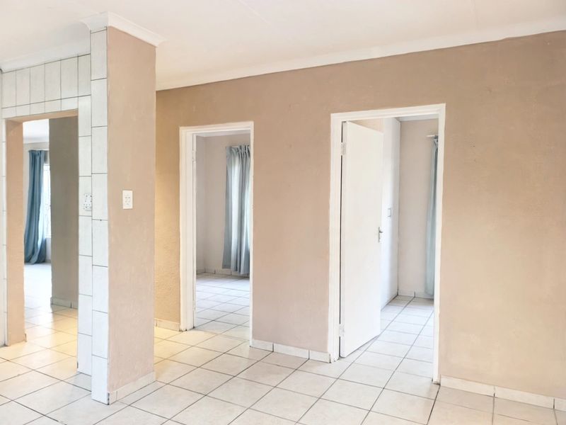 A neutral-toned hallway featuring tiled flooring and multiple doorways leading to adjacent rooms, providing a clean and functional transition space.
