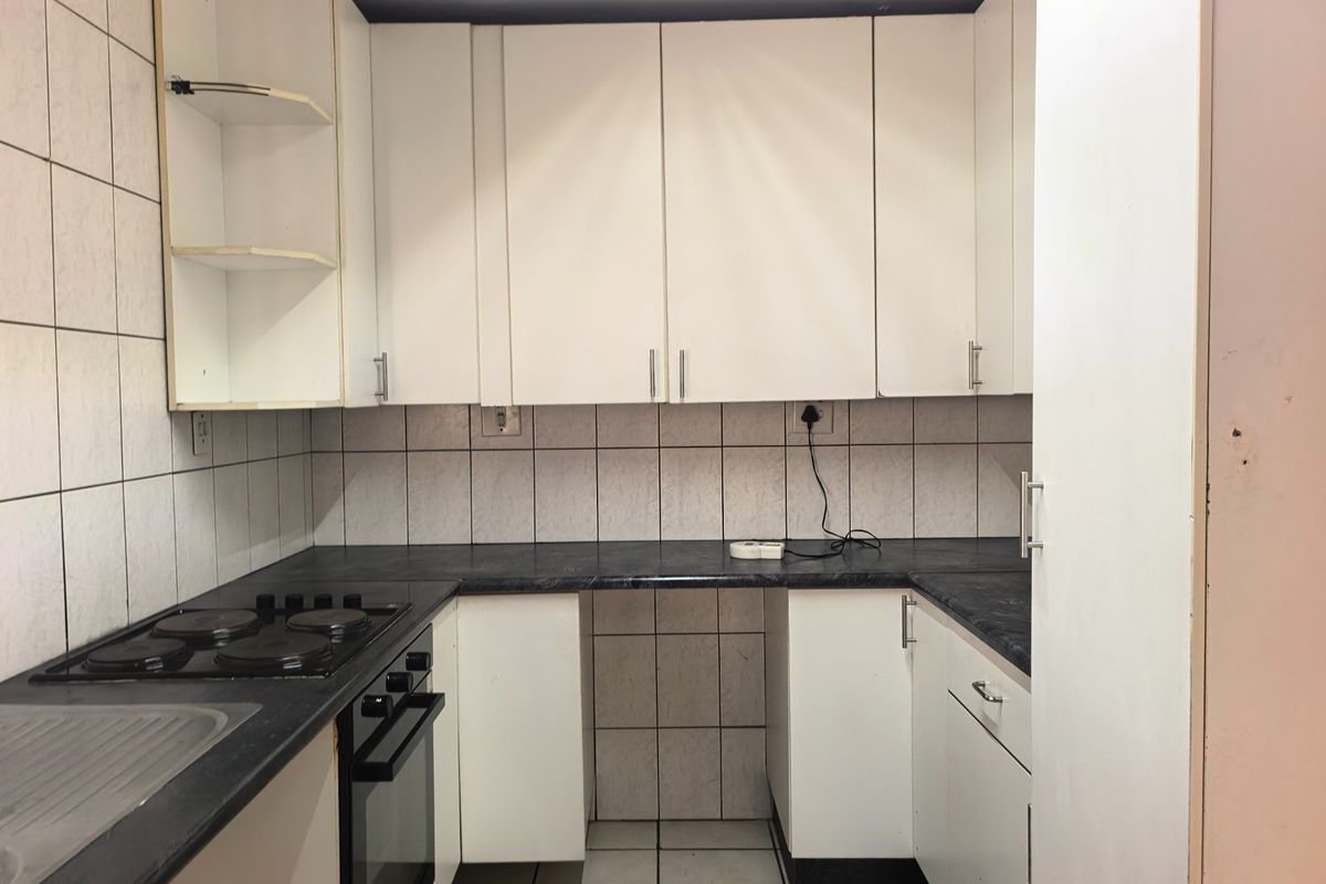 A compact kitchen featuring white cabinetry, dark laminate countertops, an integrated electric hob and oven, and tiled wall finishes.