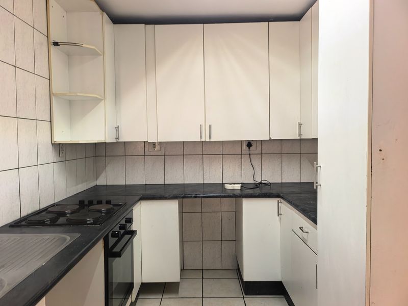 A compact kitchen featuring white cabinetry, dark laminate countertops, an integrated electric hob and oven, and tiled wall finishes.