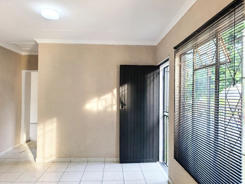 A bright, empty living area featuring neutral walls, tiled flooring, and a security gate leading to the exterior.