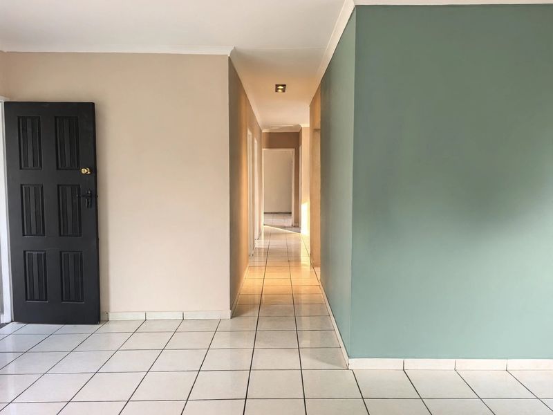 A clean, well-lit hallway featuring neutral and accent-colored walls, tiled flooring, and recessed lighting, providing a bright transition between living spaces.