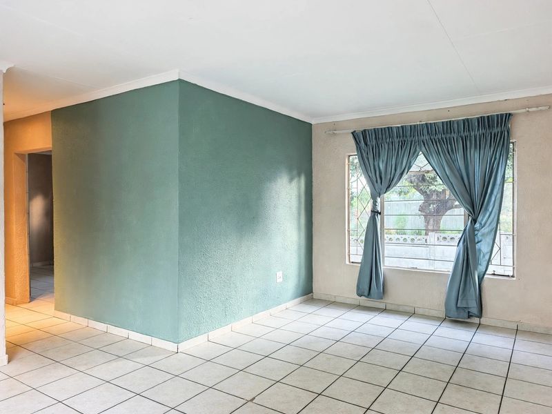 A bright, empty living area featuring tiled flooring, security bars on the window, and a distinct accent wall.
