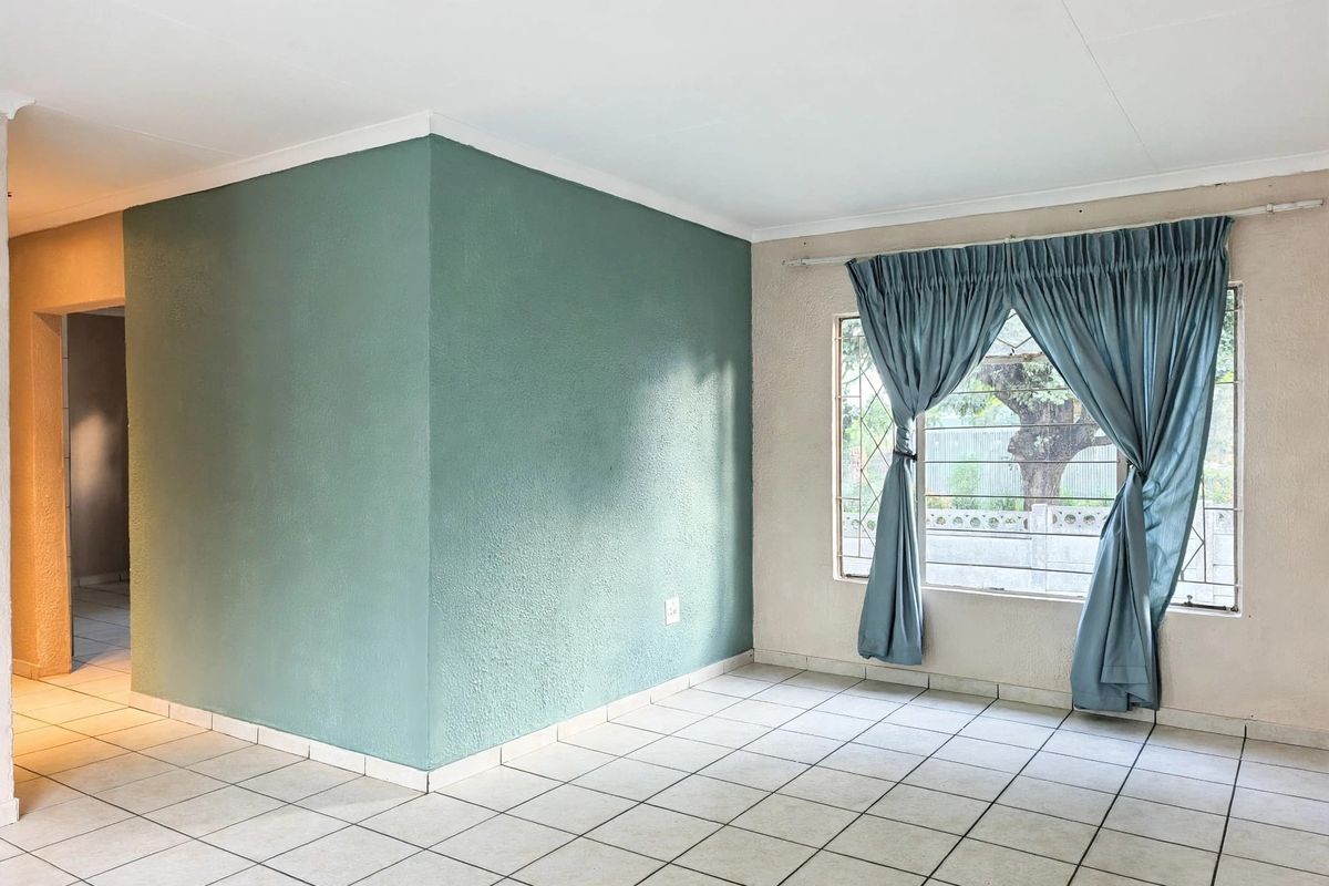 A bright, empty living area featuring tiled flooring, security bars on the window, and a distinct accent wall.