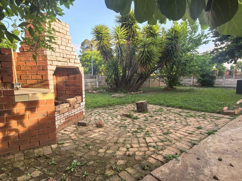 A rear garden area featuring a brick braai, paved patio space, and established lawn, offering potential for outdoor entertainment area development.