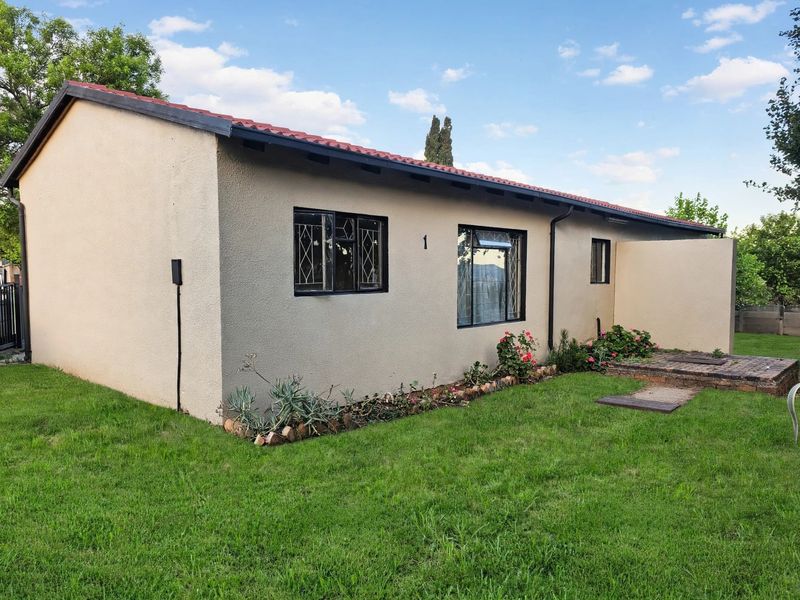 A well-maintained rear exterior view of the house featuring a tiled roof, stucco finish, security-barred windows, and a small brick-paved patio area.