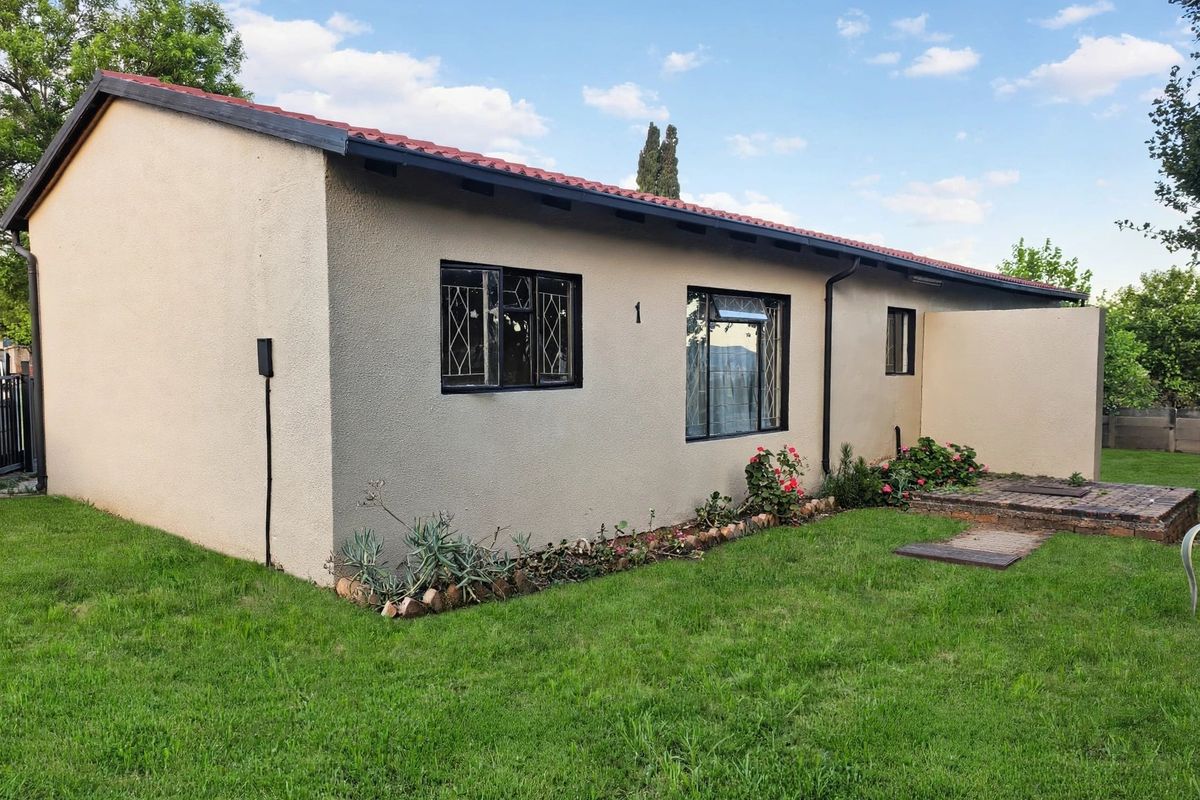 A well-maintained rear exterior view of the house featuring a tiled roof, stucco finish, security-barred windows, and a small brick-paved patio area.